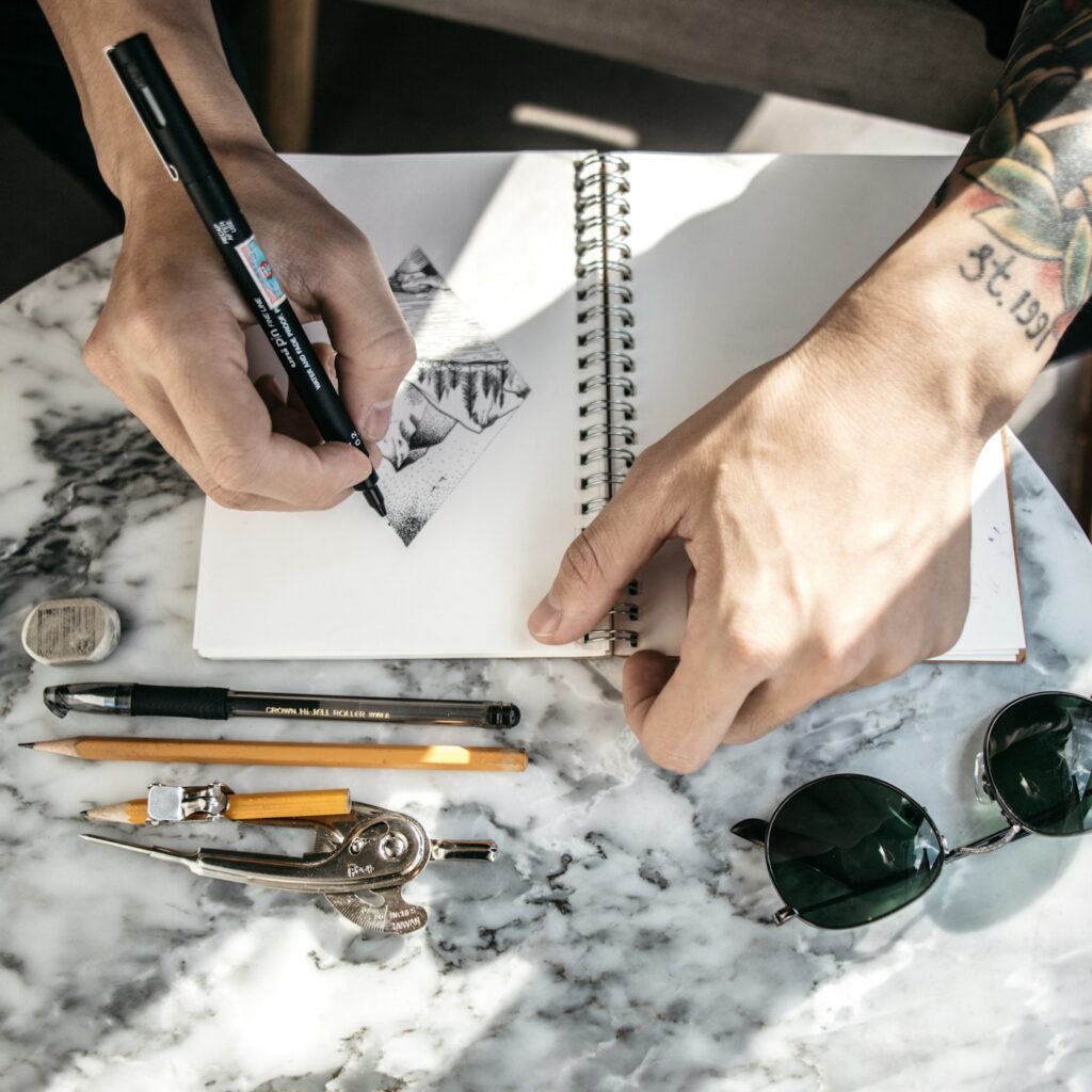 Artist sketching tattoo designs with markers in a sketchbook