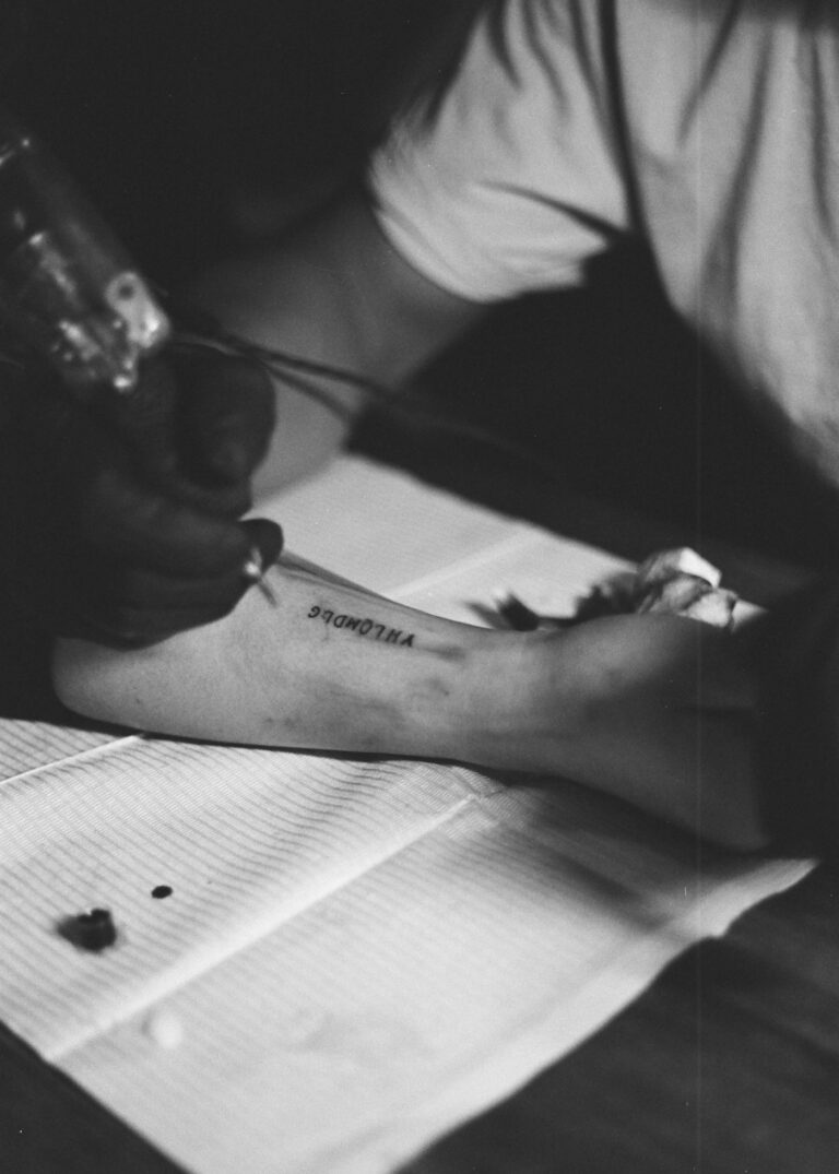 Small tattoos for guys: artist tattooing small script on an arm