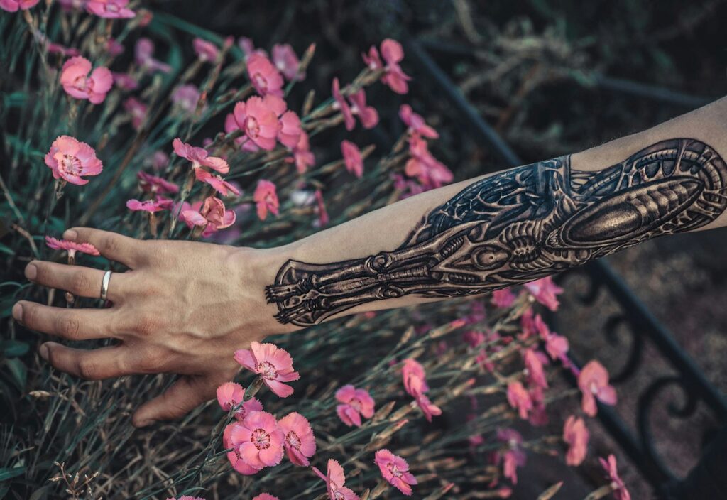 Black and white floral tattoo on a forearm among pink flowers
