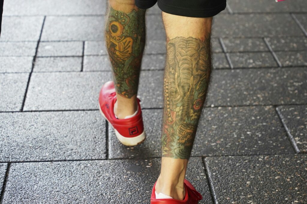 Tattoo sleeves on both calves of a man in red shoes