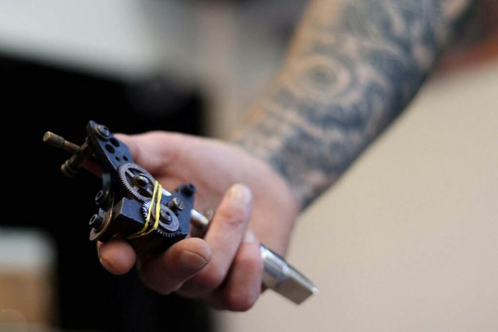 Coil tattoo machine held in a tattooed hand