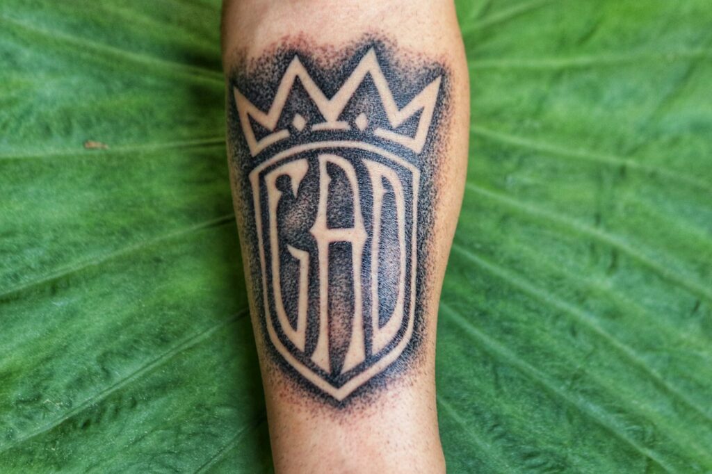 Dense black crown lettering tattoo on the forearm