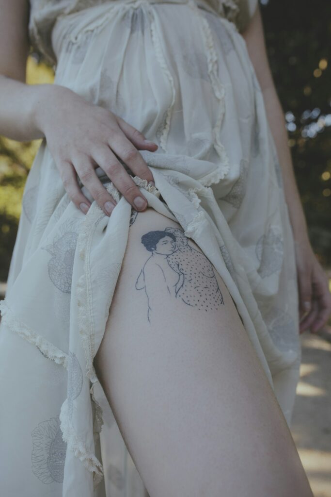 Fine line tattoo on a woman's upper thigh under a dress