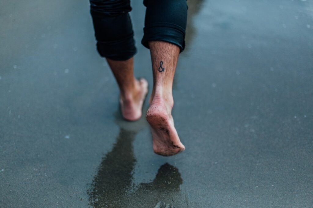 Foot tattoo on a woman walking on wet sand