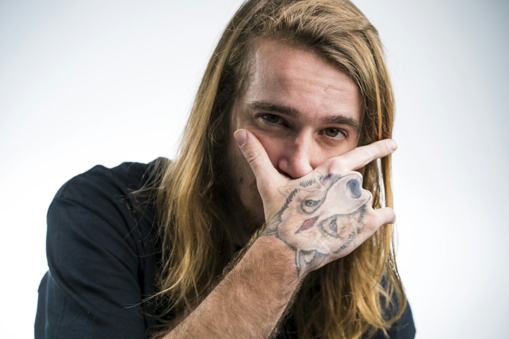 Man with long hair covering his face with a fully tattooed hand and fingers