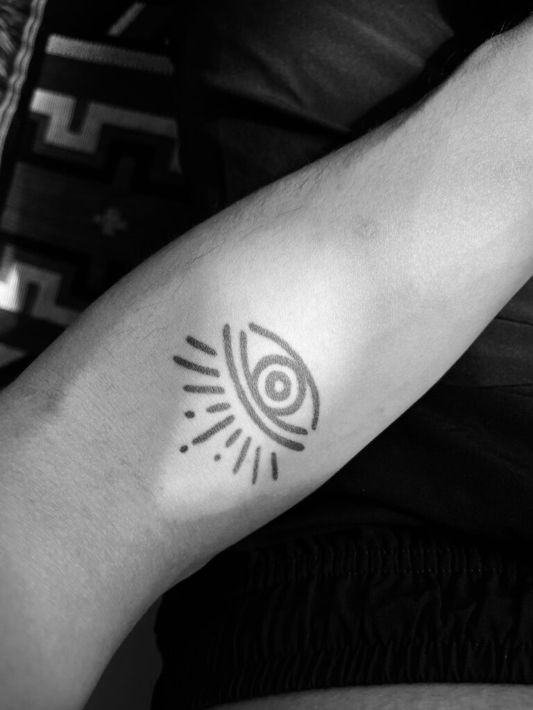 Geometric eye tattoo with rays on the forearm
