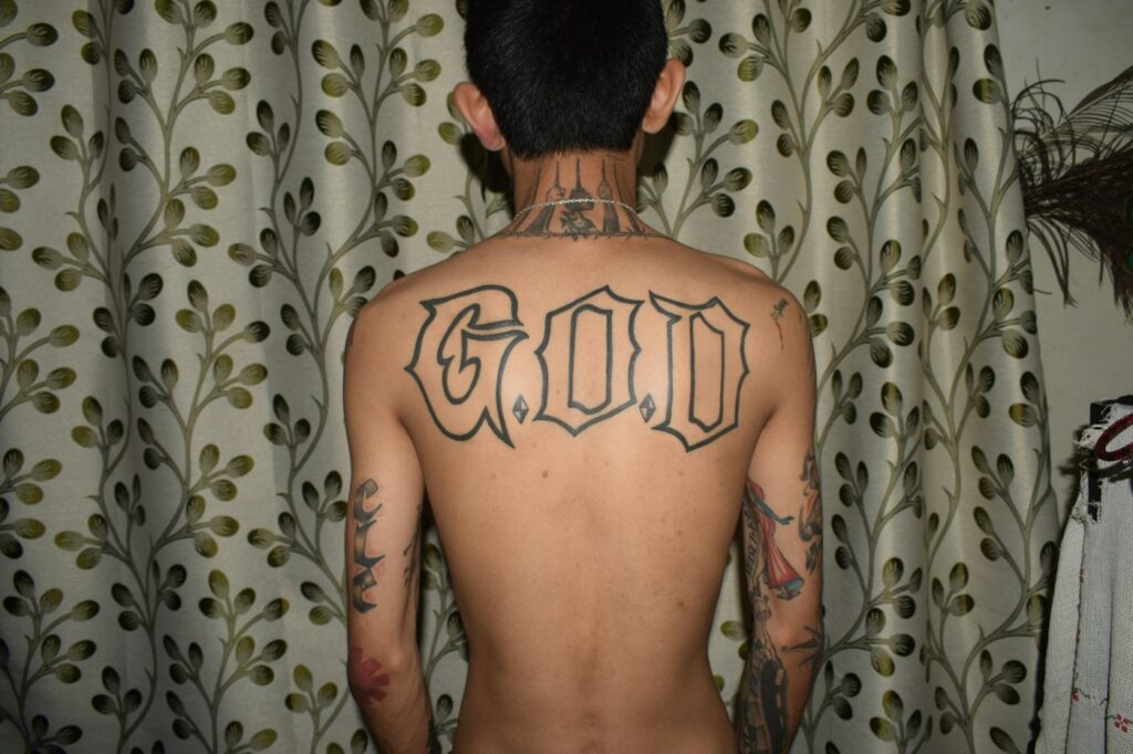 Large blackletter GOD tattoo across the upper back