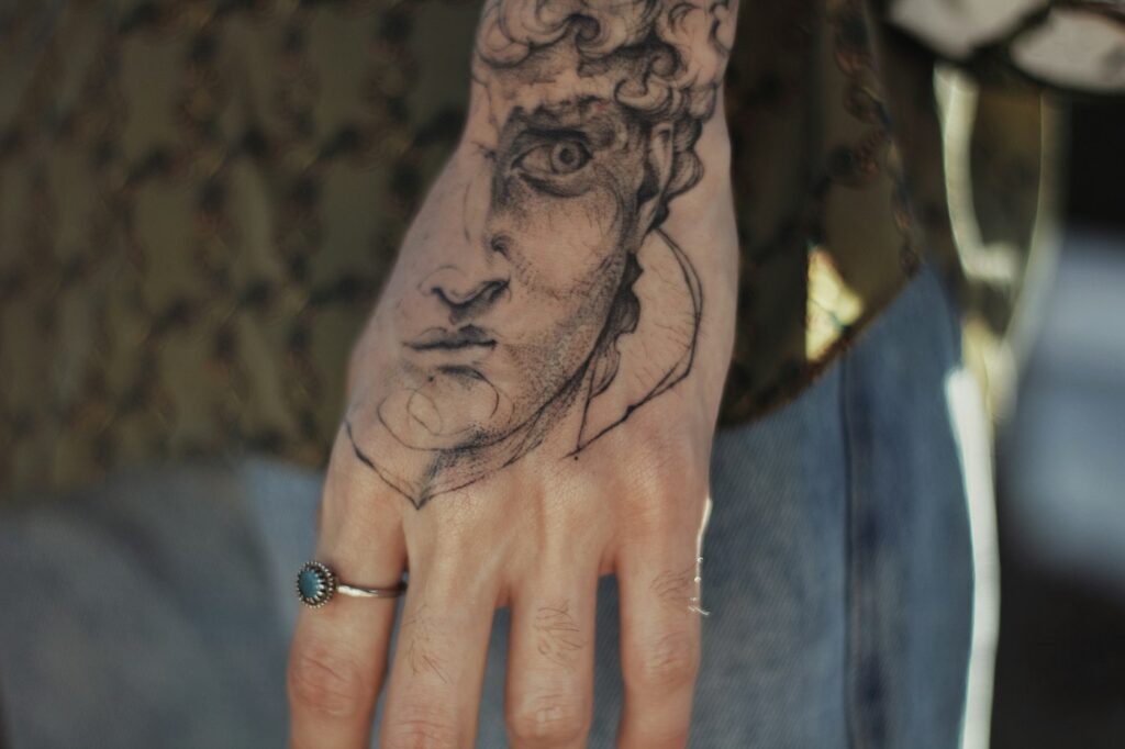 Fine line Greek statue face tattoo on the back of the hand