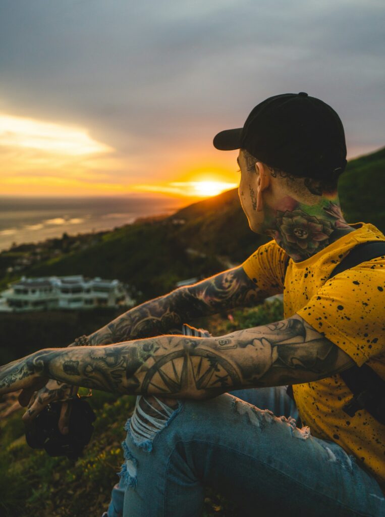 Half sleeve tattoos for men: tattooed man sitting on a hill at sunset