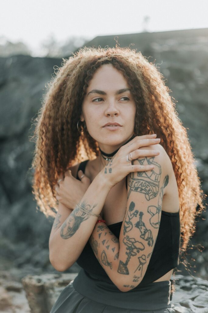 Woman with curly hair and half sleeve tattoos on both arms