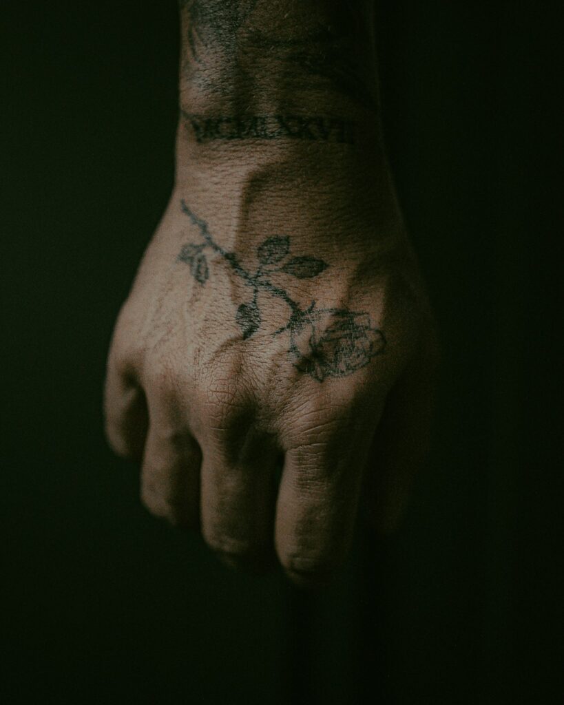 Fine line rose branch hand tattoo with script on the wrist