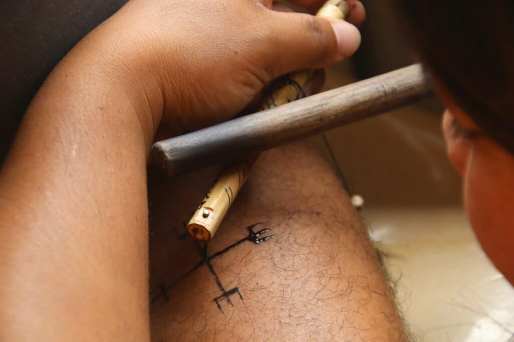 Artist using a traditional hand tool to tattoo a small symbol on the leg