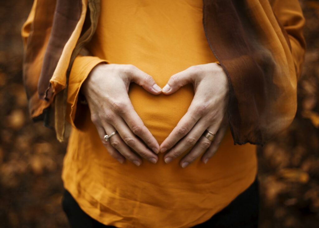 Hands forming a heart shape over a pregnant belly