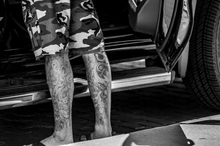Leg tattoos for men: tattooed man standing next to a car