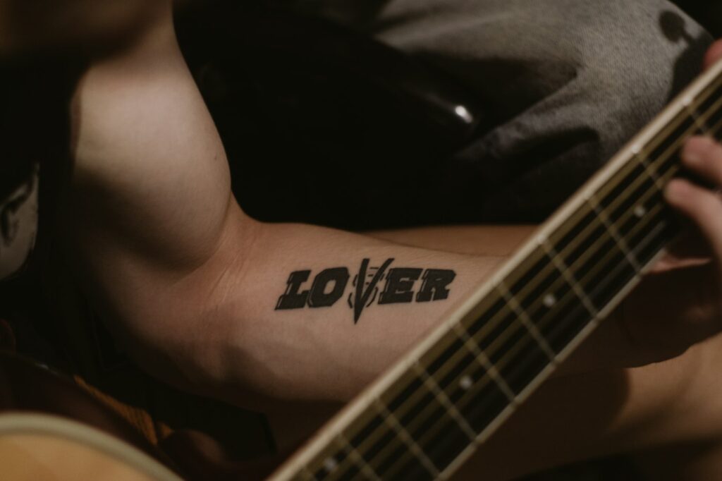 Bold LOVER lettering tattoo on the forearm of a guitarist
