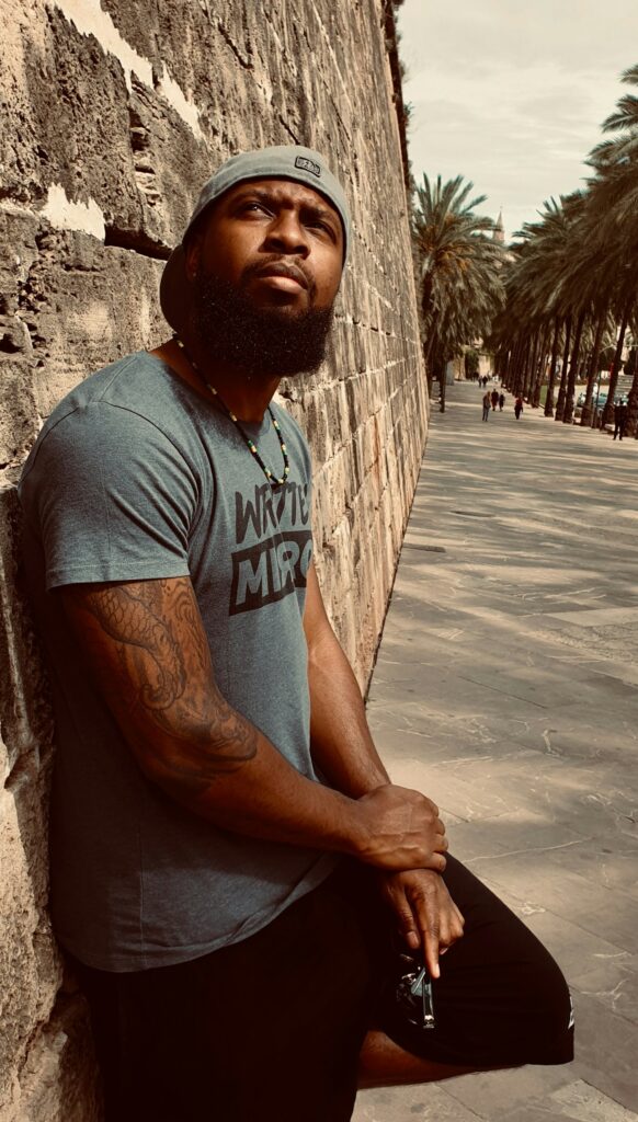 Man with black and grey arm tattoos leaning on a stone wall