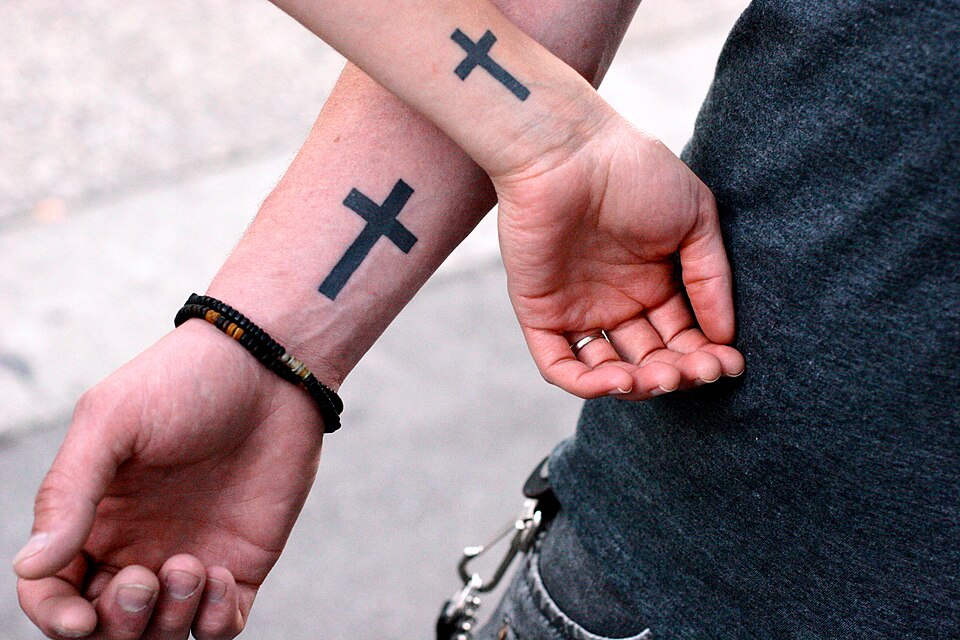 Matching black cross tattoos on two wrists