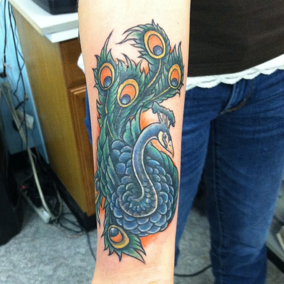 Colorful peacock cover up tattoo on the forearm