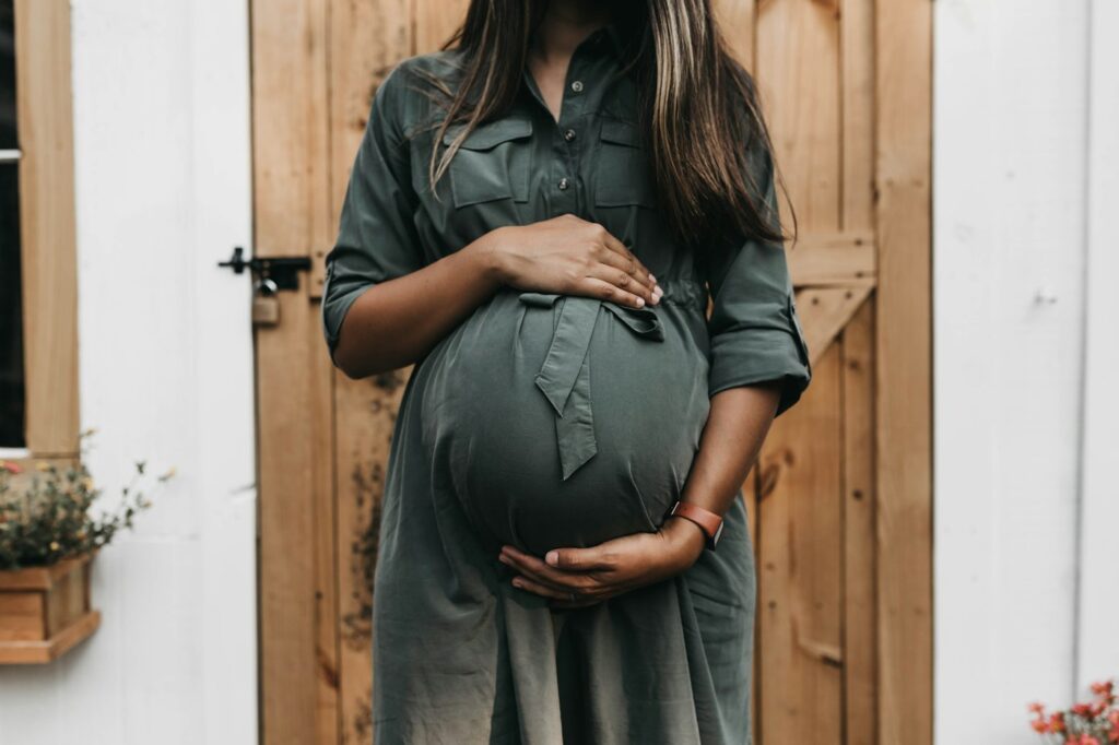 Pregnant woman in a grey dress holding her belly