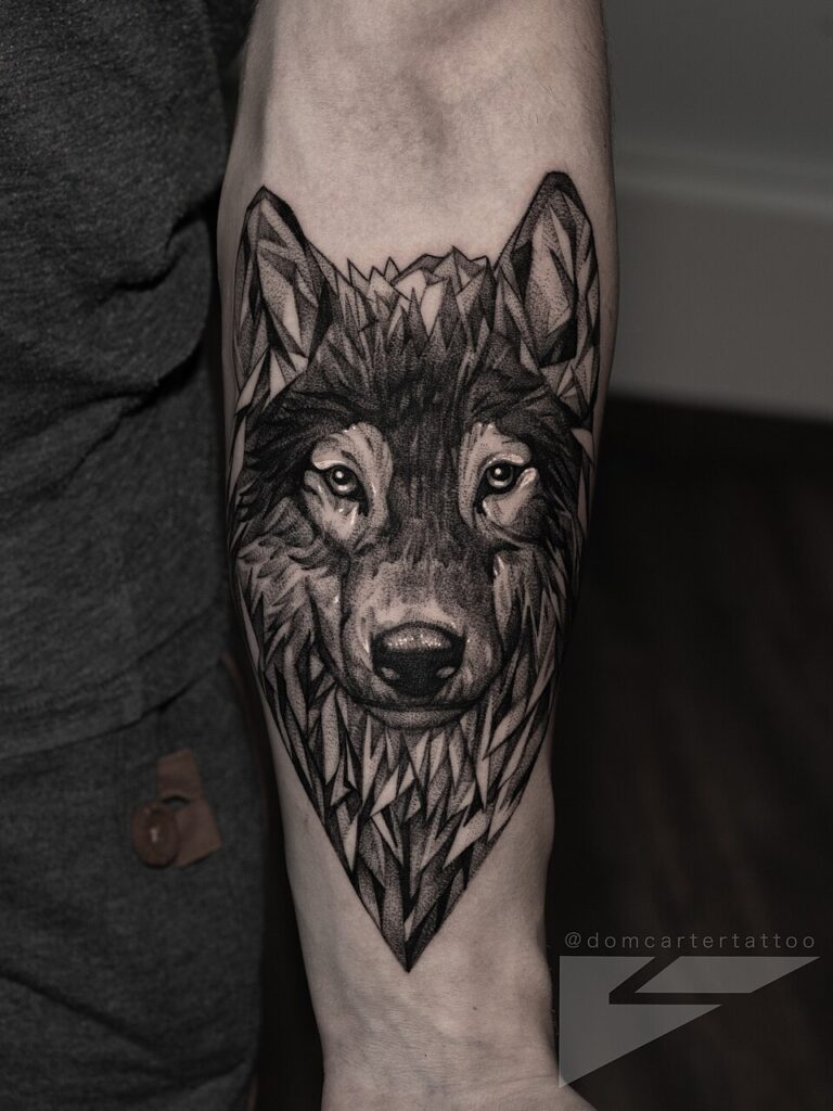 Realistic black and grey wolf head forearm tattoo in a diamond frame