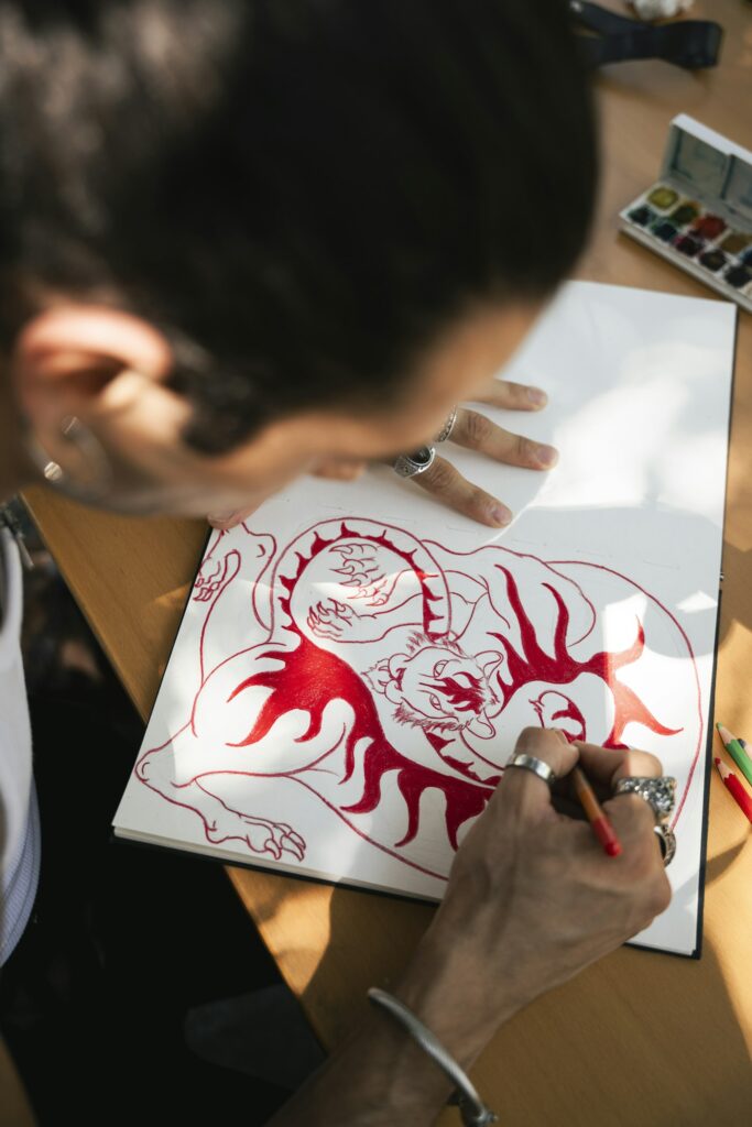 Artist sketching a red dragon tattoo design on paper