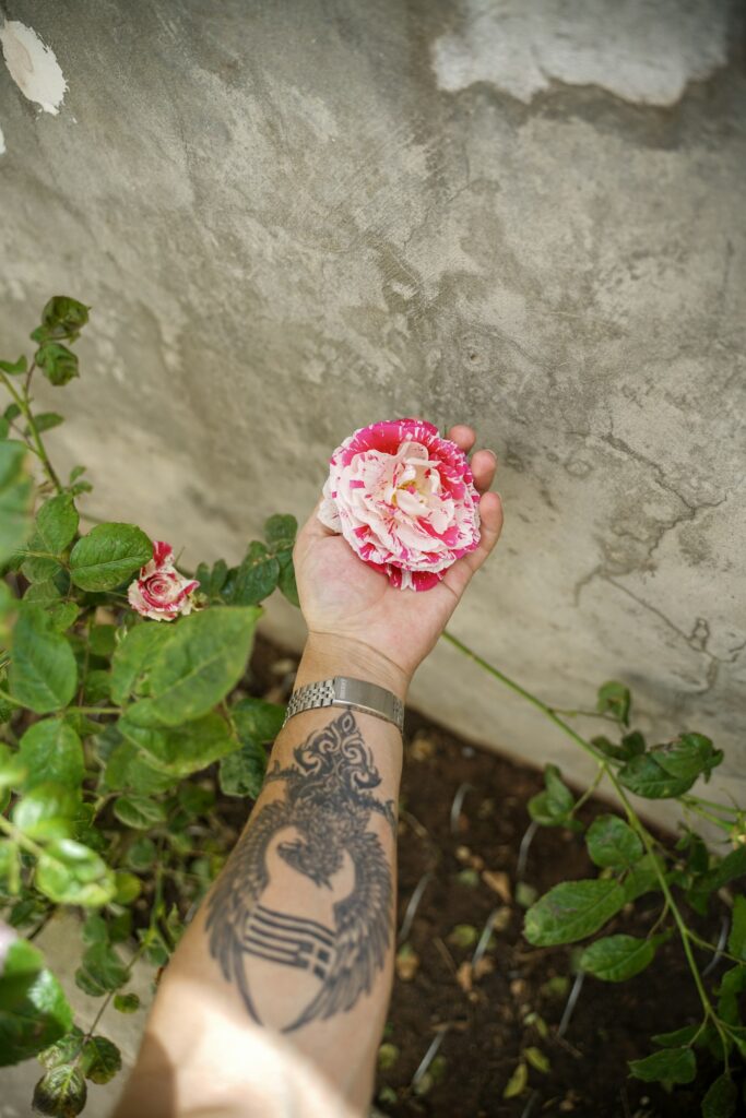 Floral forearm tattoo on a hand holding a pink rose
