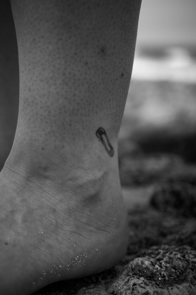 Tiny safety pin tattoo on the ankle