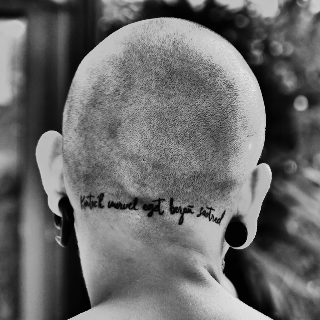 Script quote tattoo across the back of the neck