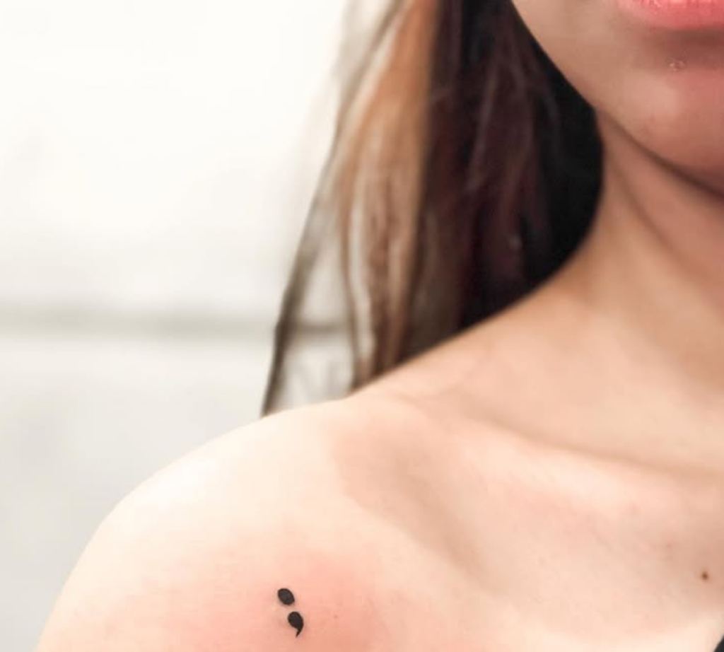 Small semicolon tattoo on the shoulder near the collarbone