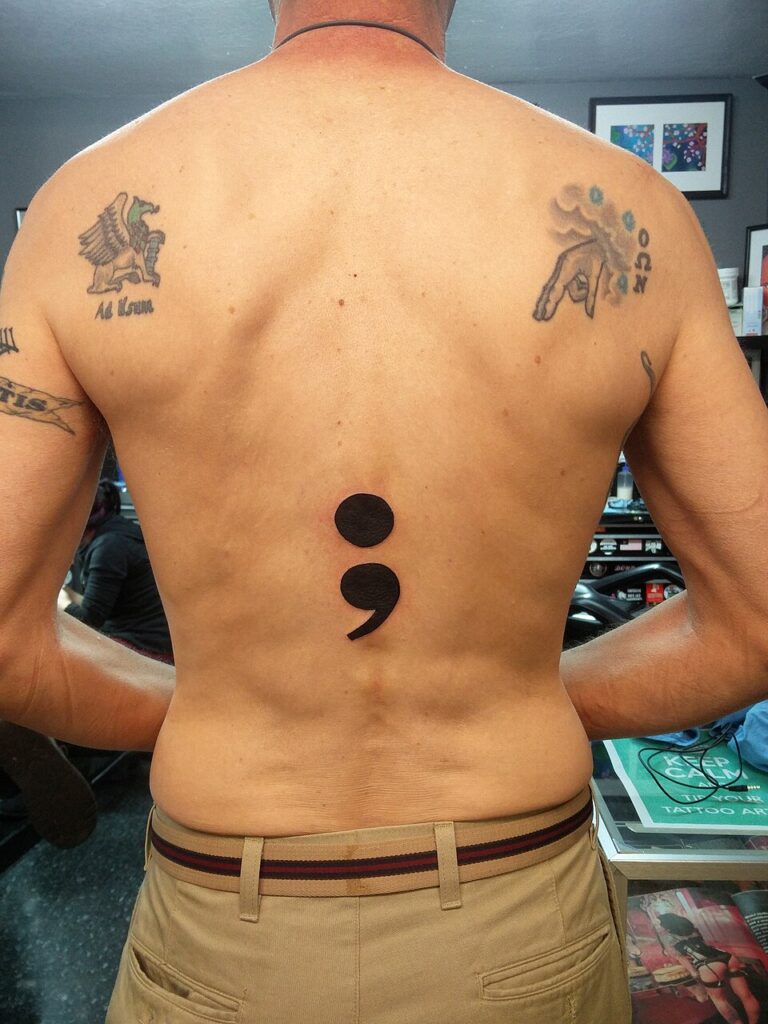 Large semicolon tattoo on the spine of a man's back