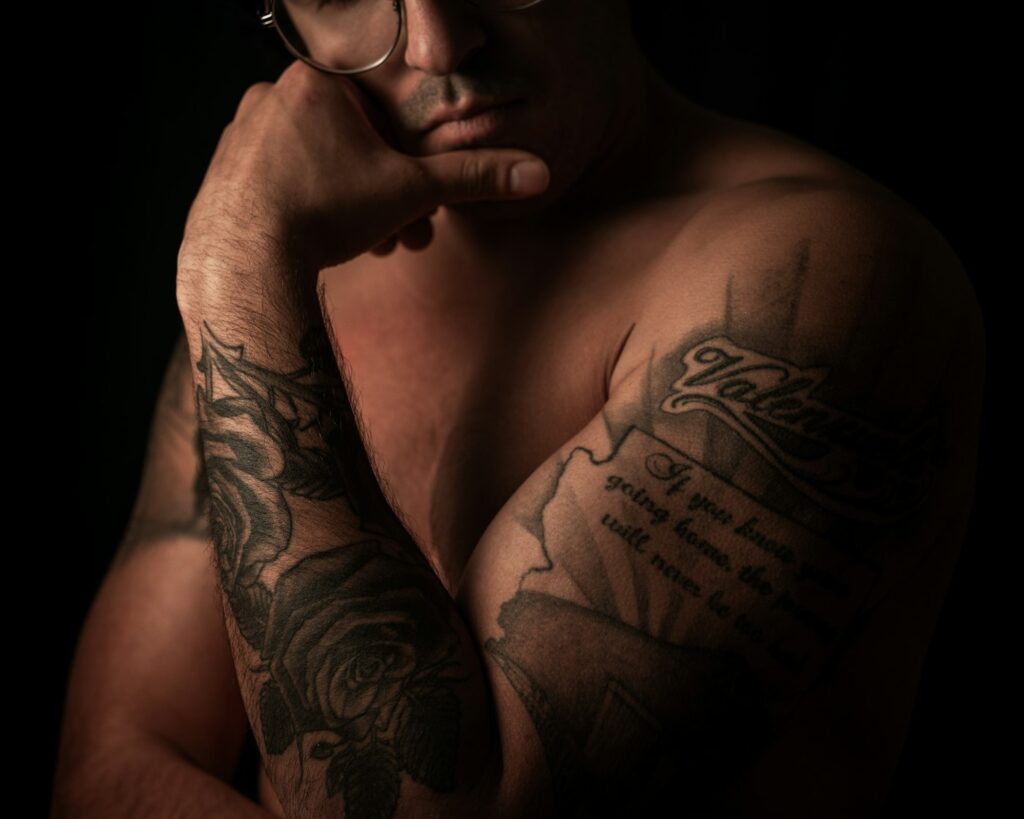 Script and black and grey tattoos across a man's shoulder and chest