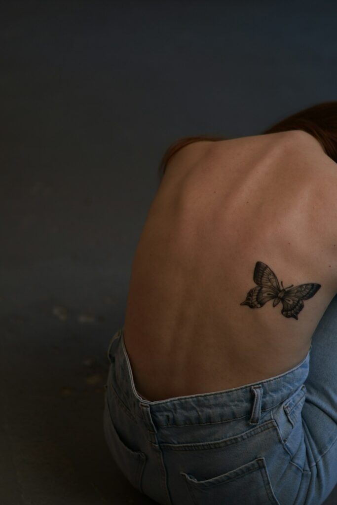 Small butterfly tattoo between the shoulder blades