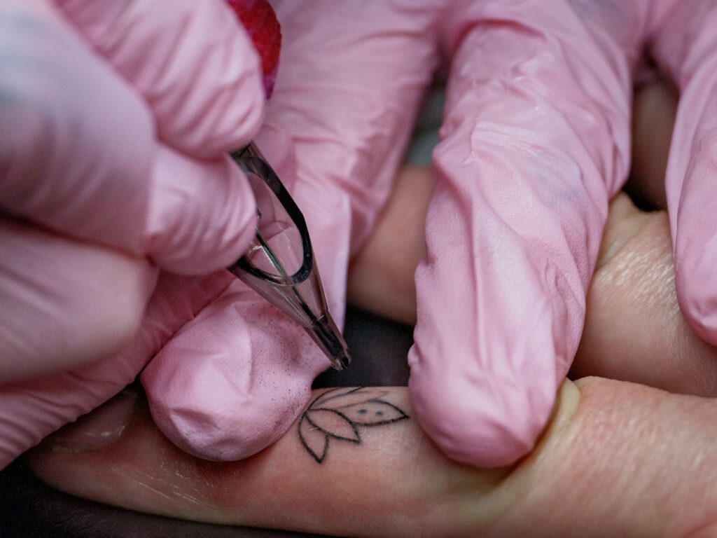 Lotus tattoo: small fine line lotus on the hand being inked