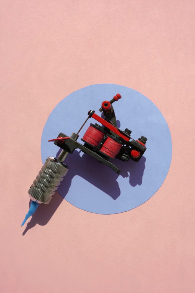Tattoo gun: red coil tattoo machine on a pink and blue background