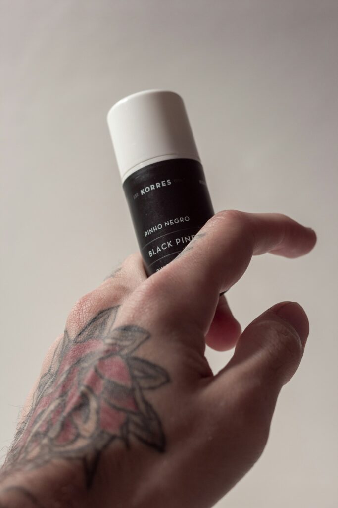 Tattoo scabbing care: tattooed hand holding a bottle of aftercare balm