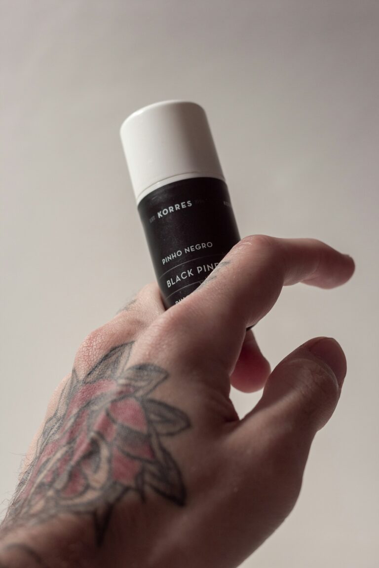 Tattoo scabbing care: tattooed hand holding a bottle of aftercare balm
