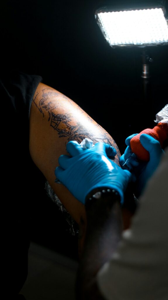 Tattoo artist in blue gloves working on a deep skin tone