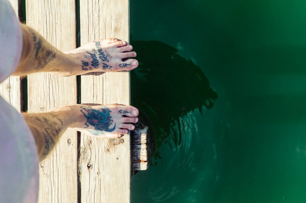 Tattooed feet on a wooden dock above lake water