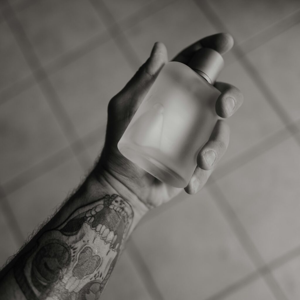 Tattooed forearm in black and white holding a glass bottle