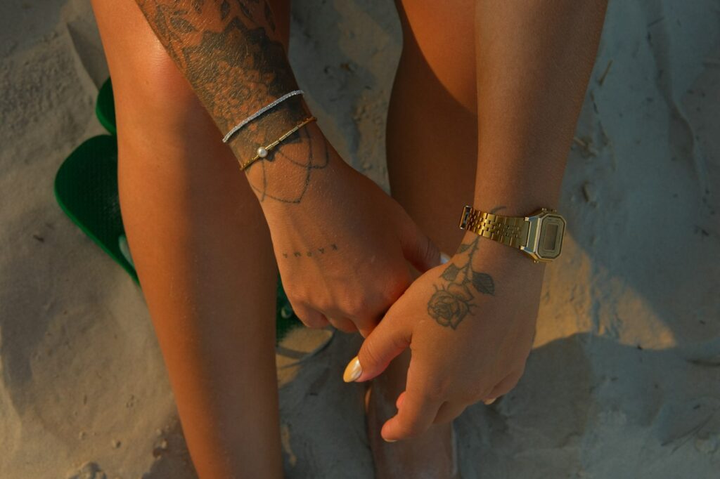 Tattooed hands and wrists with bracelets on beach sand