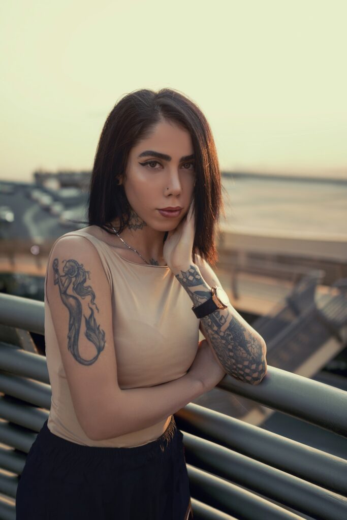 Woman with tattoos on both arms leaning on a railing