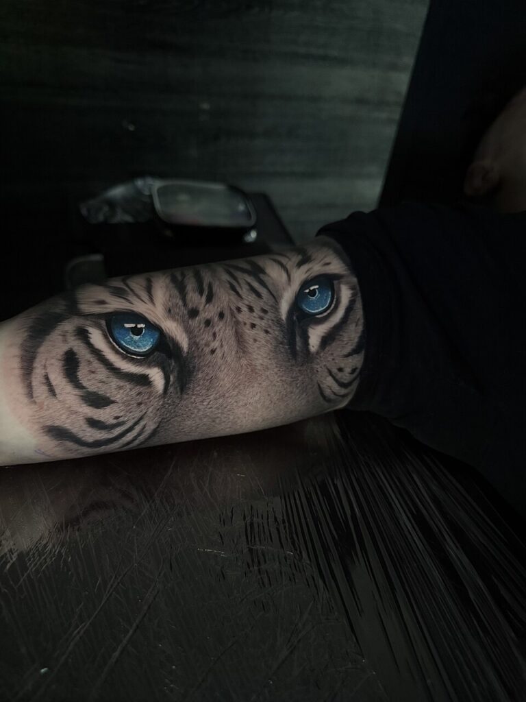 Realistic tiger eyes tattoo wrapping around the forearm