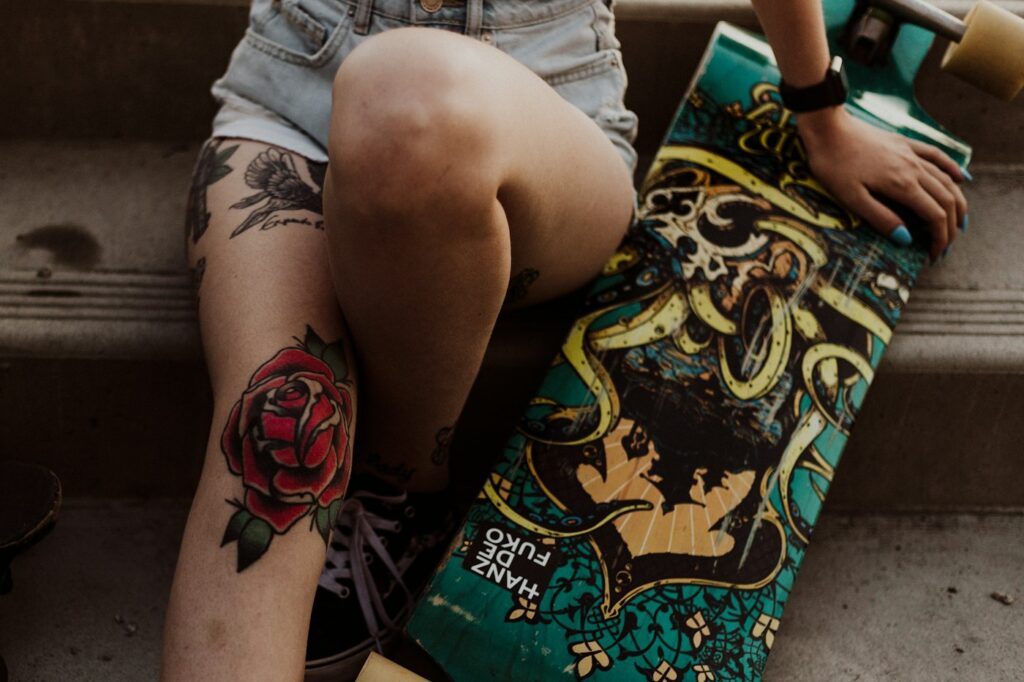 Traditional red rose calf tattoo on a woman holding a longboard