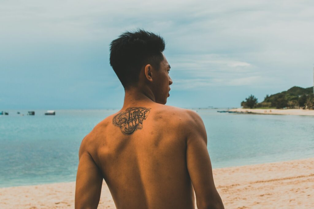 Upper back tattoo on a man standing on the beach