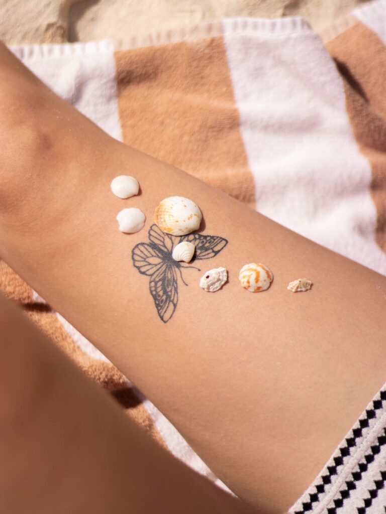 Butterfly tattoo on the lower leg with seashells on the sand