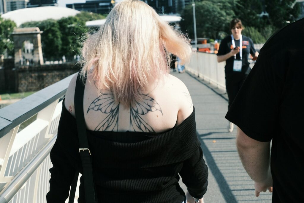 Fine line butterfly wings tattooed across the upper back