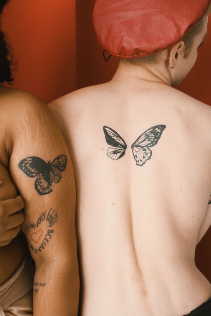Two people showing matching butterfly tattoos on their backs