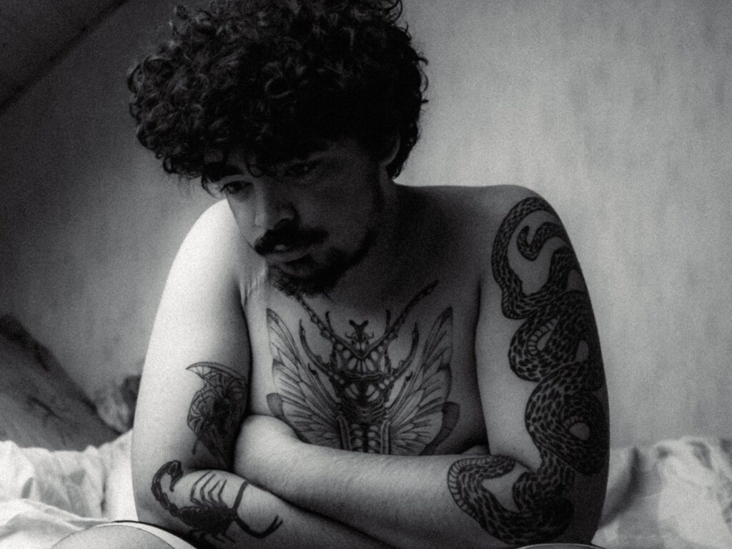 Man with a moth tattoo on his chest and a tattooed arm