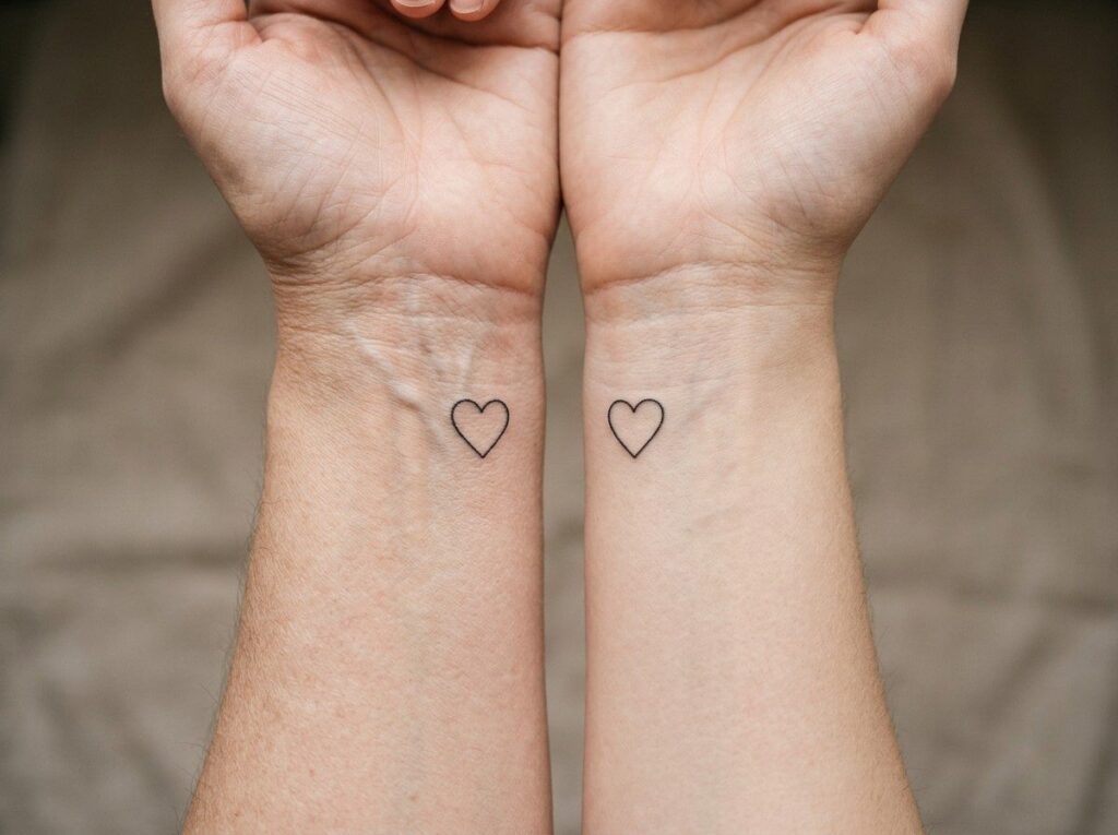 Mother daughter tattoos: matching fine line hearts on two wrists